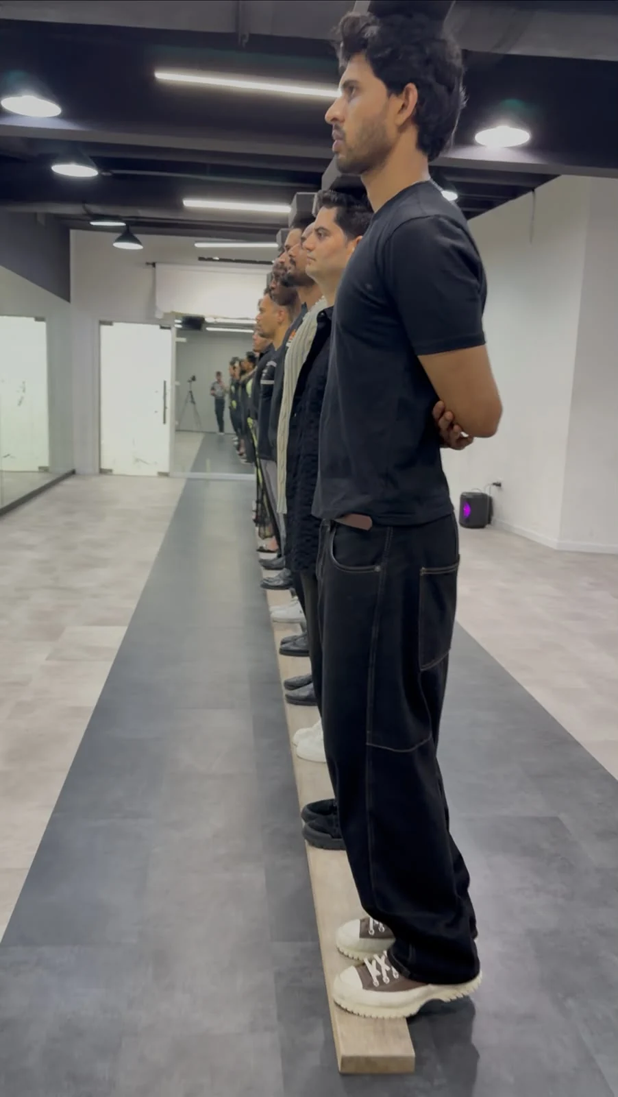 A line of models practising posture in a mirrored studio.