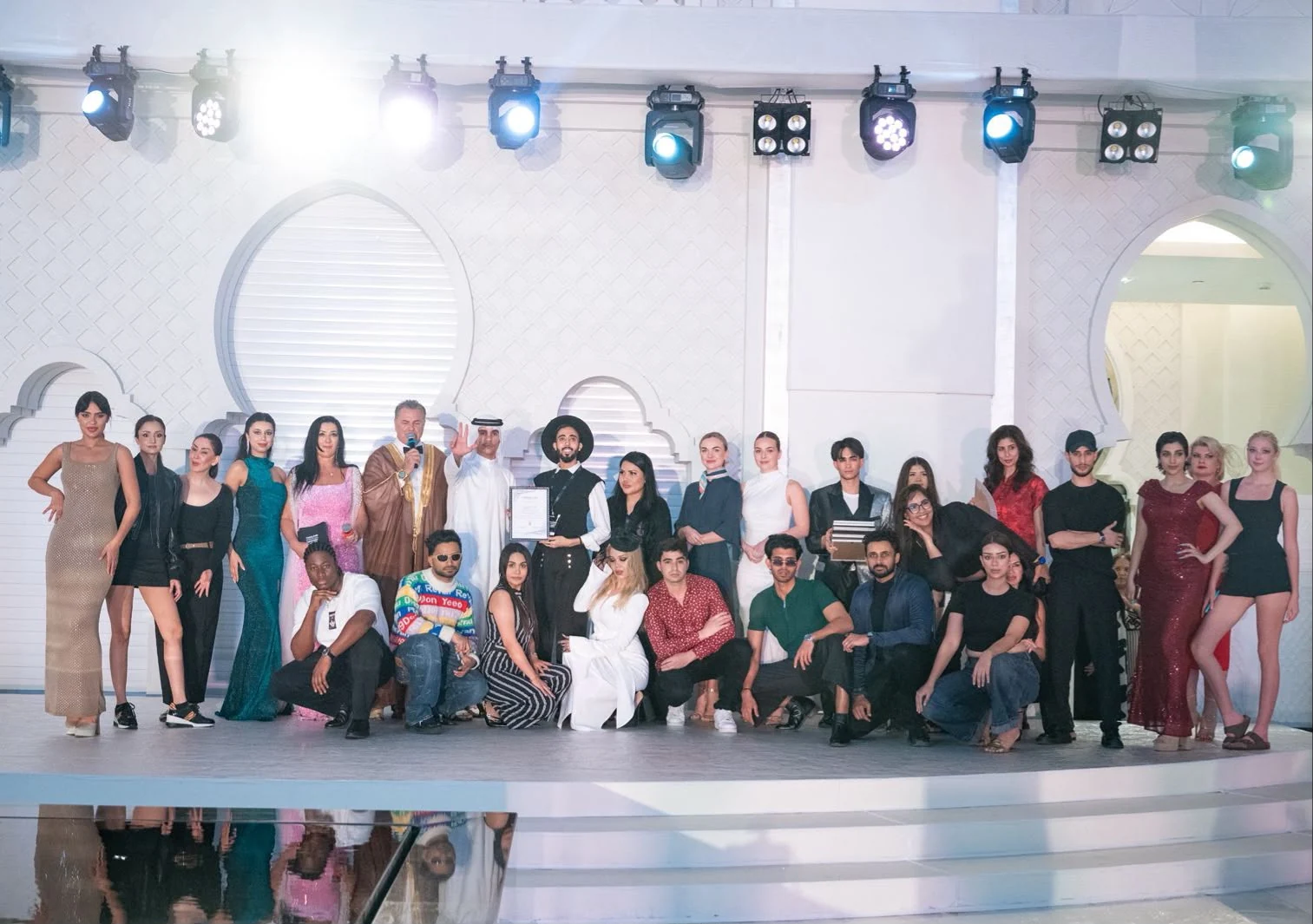 Models and event participants posing together on a fashion-show stage.